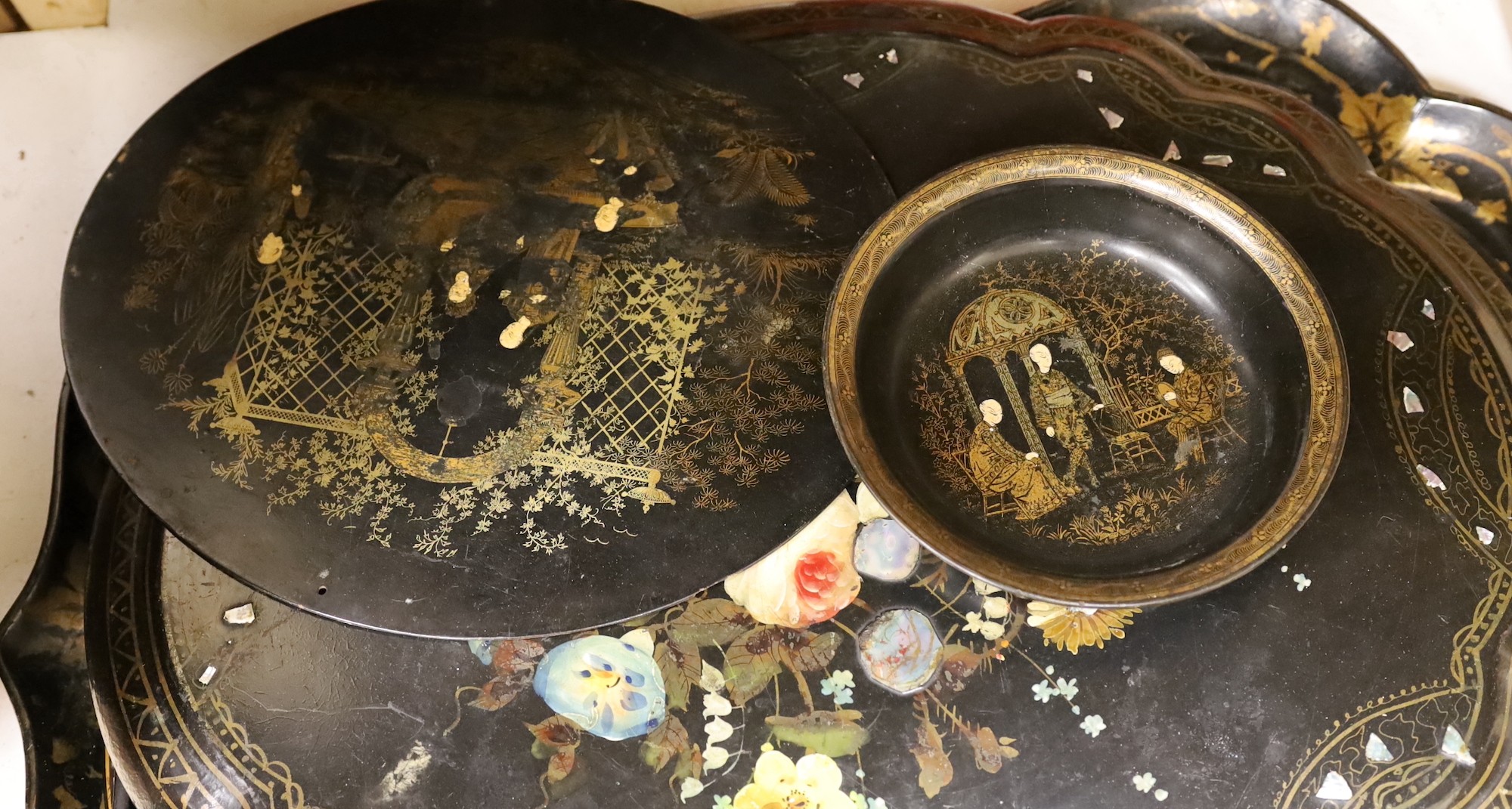 Four papier-mâché-mâché trays, a roundel and bowl, largest tray 80cms wide